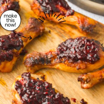 Baked chicken drumsticks with a glossy blackberry glaze arranged on a wooden board, garnished with a text overlay promoting the recipe and the website thetastesoflife.com.
