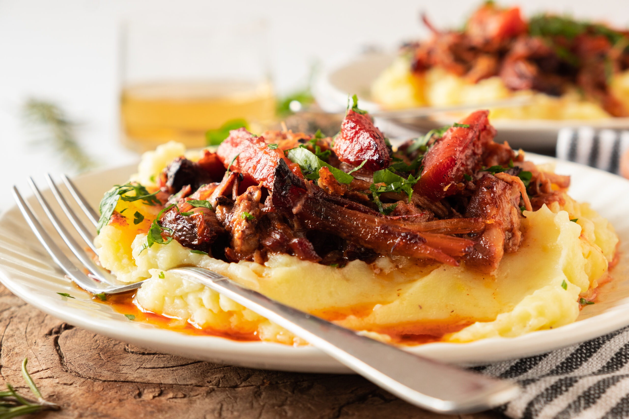 Slow-Cooked Pork Pot Roast topped with fresh herbs served over a bed of mashed potatoes on a white plate with a fork.