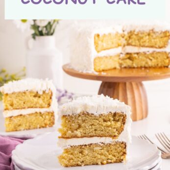 A slice of Gluten-Free Dairy-Free Coconut Cake rests on stacked plates before the remaining cake on a wooden stand, accented by white flowers and a purple napkin. Text reads: GLUTEN-FREE DAIRY-FREE COCONUT CAKE.