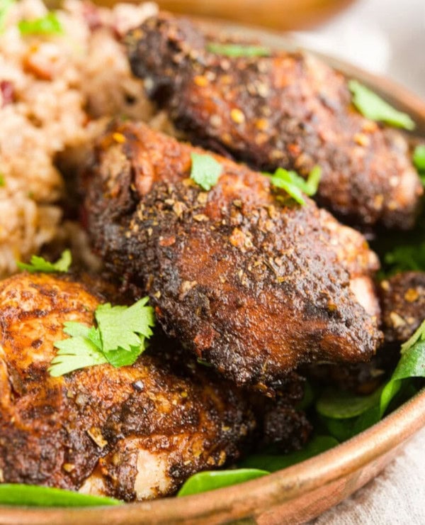 A close-up of seasoned, baked chicken thighs garnished with fresh cilantro, served with a side of rice on a plate.