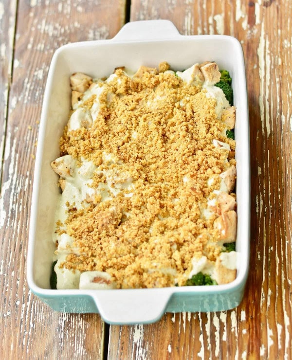 A casserole dish A Roundup Image for Delicious Dinner Recipes with a baked dish topped with a golden breadcrumb crust. Chunks of chicken and pieces of broccoli are visible under the crust, sitting on a rustic wooden table.