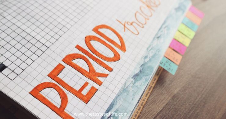 A close-up of a grid notebook with PERIOD tracker written in large orange letters. Colorful tab markers are visible on the right edge of the page. The notebook rests on a wooden surface.