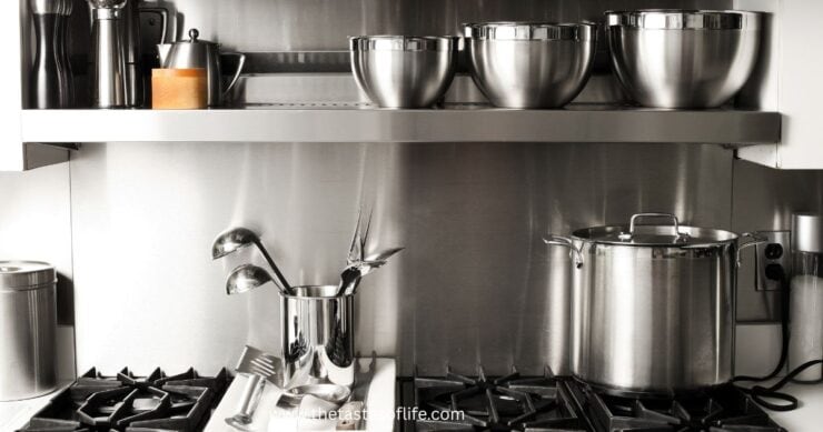 A modern kitchen with stainless steel cookware, including mixing bowls, a large pot on the stove, and utensils in a holder, all set against a shiny metal backsplash.